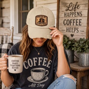 May include: A beige distressed baseball cap with a rectangular patch featuring a coffee cup graphic and the text Fueled By Coffee. The cap is paired with a dark gray t-shirt displaying a coffee cup illustration and the text Coffee All Day.