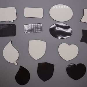 May include: Assortment of blank sublimation blanks in various shapes, including a speech bubble, rectangle, oval, star, leaf, shield, and heart. The blanks are white and black.