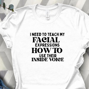 May include: White t-shirt with black text that reads "I need to teach my facial expressions how to use their inside voice."