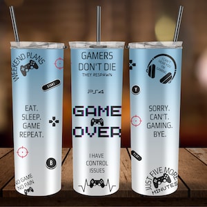 May include: Three blue and white stainless steel tumblers with gamer-themed designs. The tumblers feature phrases like "Weekend Plans", "Gamers Don't Die", "I Can't Hear You I'm Gaming", "Game Over", "Just Five More Minutes", and "No Game No Pain".