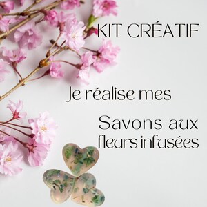 Peut inclure: Un kit créatif avec le texte "KIT CRÉATIF" et "Je réalise mes Savons aux fleurs infusées". L'image présente trois savons en forme de cœur avec des inclusions florales, sur fond blanc avec des branches de fleurs de cerisier roses.