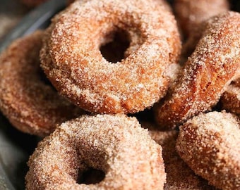 Puede incluir: Primer plano de varios donuts cubiertos de azúcar y canela sobre un plato plateado. Los donuts son de color marrón dorado con una generosa capa de azúcar y canela. Algunos tienen un agujero en el centro, otros son agujeros de donut.