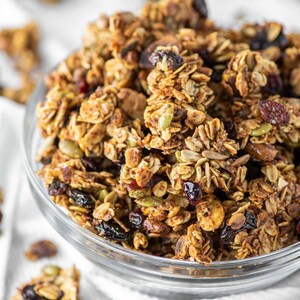 May include: A glass bowl filled with homemade granola. The granola is made with oats, nuts, seeds, and dried fruit. It is a healthy and delicious breakfast or snack option.