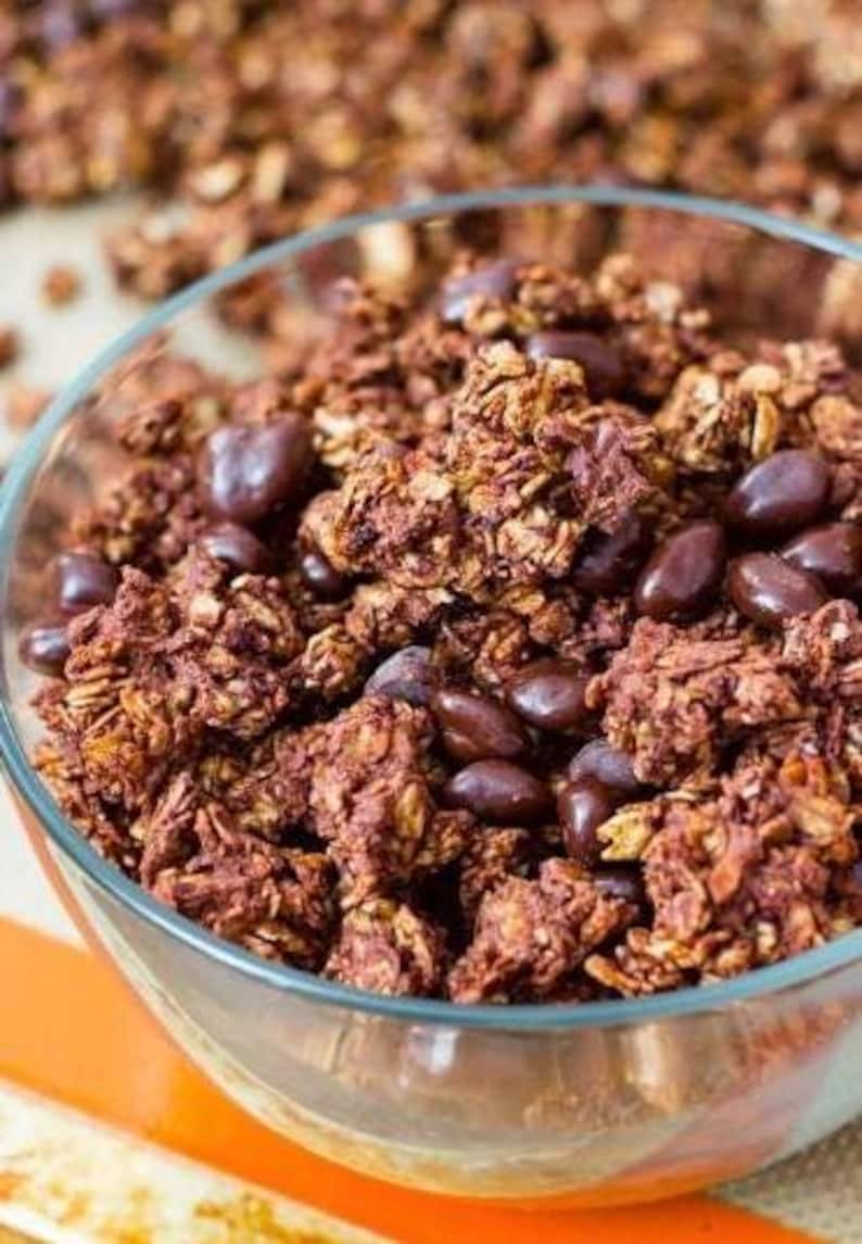 May include: A glass bowl filled with chocolate granola and chocolate chips. The granola is a dark brown color and the chocolate chips are a light brown color.