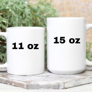 Op de afbeelding: Twee witte keramische mokken met zwarte tekst. De kleinere mok is 11 oz en de grotere mok is 15 oz.