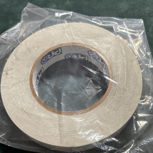 May include: A roll of white double-sided adhesive tape encased in a clear plastic bag. The inner cardboard core features the text PRO printed in blue and black lettering repeatedly around the circumference of the center hole.
