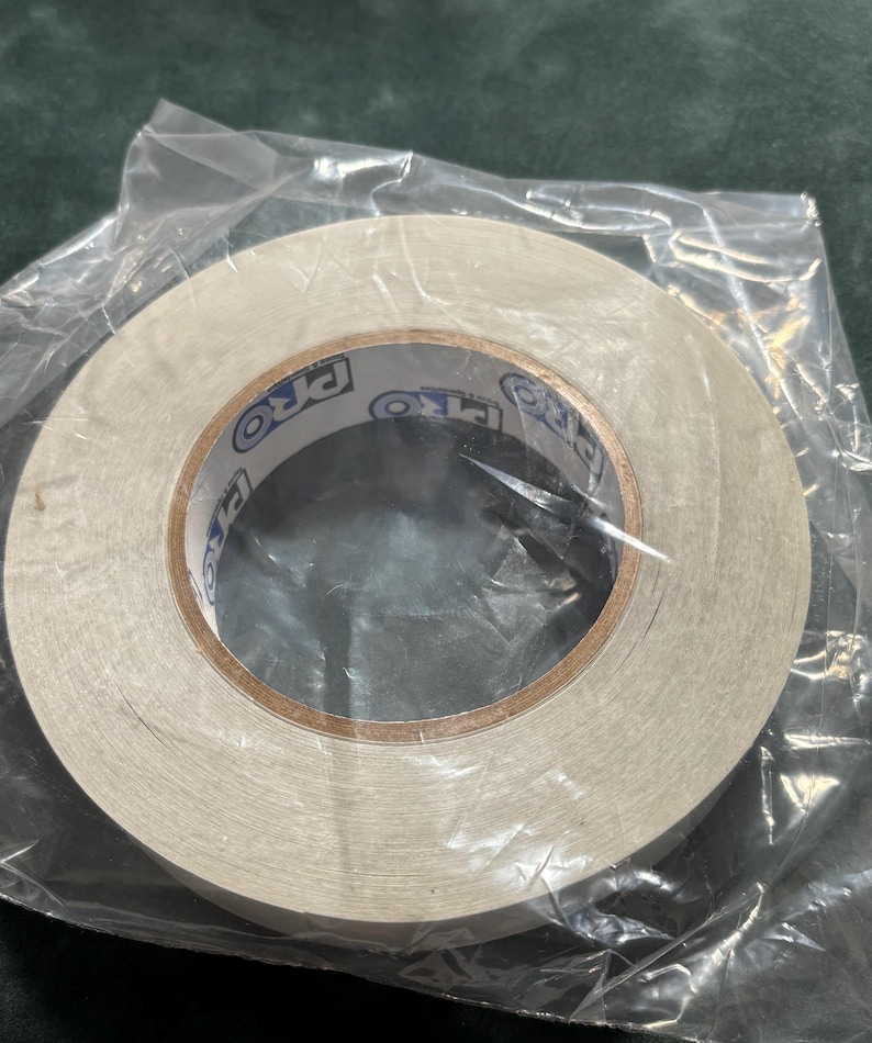May include: A roll of white double-sided adhesive tape encased in a clear plastic bag. The inner cardboard core features the text PRO printed in blue and black lettering repeatedly around the circumference of the center hole.