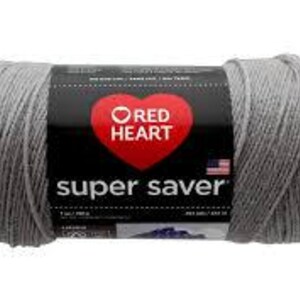 May include: A skein of light gray yarn with a black paper label featuring a red heart logo and the text Red Heart Super Saver. The label includes a small American flag icon and indicates a net weight of 7 ounces or 198 grams for the yarn.