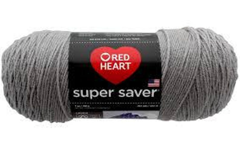 May include: A skein of light gray yarn with a black paper label featuring a red heart logo and the text Red Heart Super Saver. The label includes a small American flag icon and indicates a net weight of 7 ounces or 198 grams for the yarn.