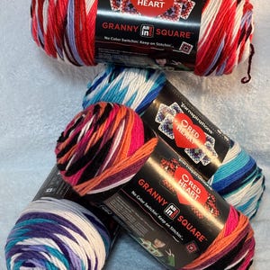 Pode incluir: Quatro novelos de fio Red Heart Granny All In One Square com r&oacute;tulos pretos. O fio apresenta padr&otilde;es de cores variadas, incluindo vermelho, branco, roxo, azul, laranja e preto. Cada r&oacute;tulo exibe o log&oacute;tipo da marca e o texto.