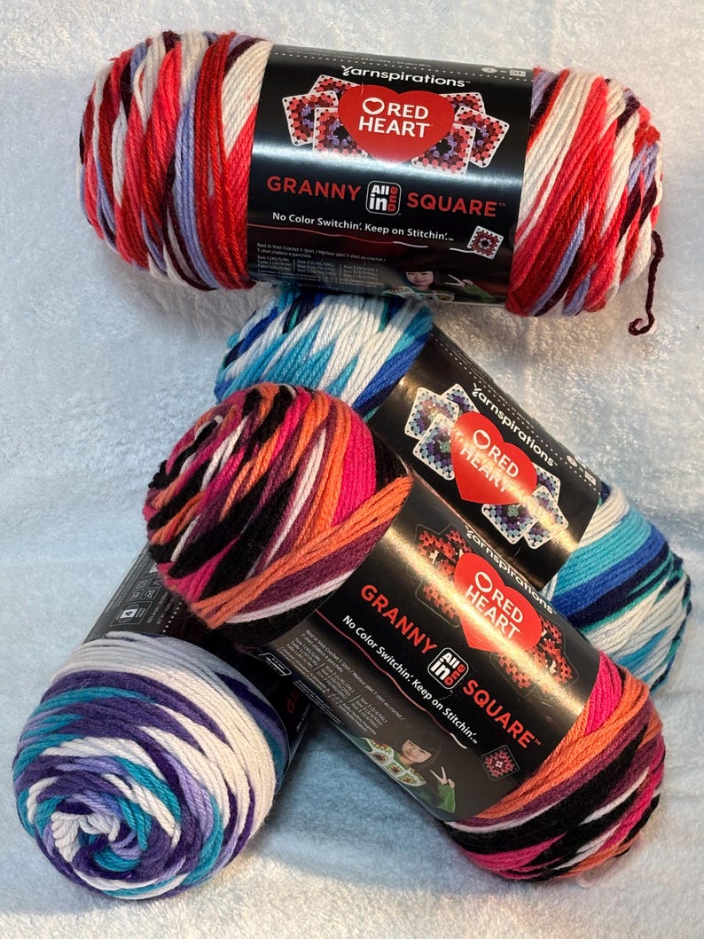 Pode incluir: Quatro novelos de fio Red Heart Granny All In One Square com r&oacute;tulos pretos. O fio apresenta padr&otilde;es de cores variadas, incluindo vermelho, branco, roxo, azul, laranja e preto. Cada r&oacute;tulo exibe o log&oacute;tipo da marca e o texto.