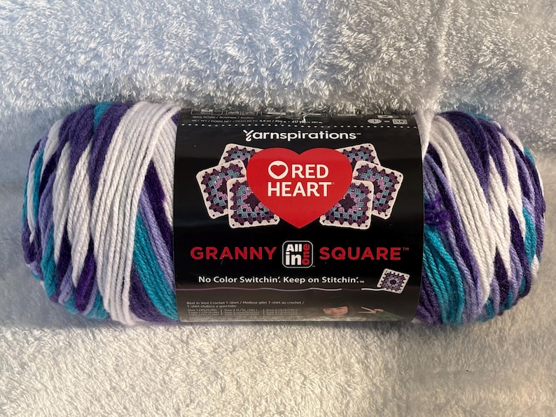 Pode incluir: Um novelo de fio Red Heart All in One Granny Square com uma paleta de cores variadas em branco, roxo claro, roxo escuro e azul-petr&oacute;leo. O r&oacute;tulo preto exibe o log&oacute;tipo da marca, um cora&ccedil;&atilde;o vermelho e o texto Granny Square.