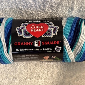 Pode incluir: Um novelo de fio Red Heart Granny All in One Square com uma paleta de cores variadas em branco, azul claro, azul m&eacute;dio e azul escuro. O r&oacute;tulo preto do produto exibe o nome da marca, o log&oacute;tipo e o texto No Color Switchin'.