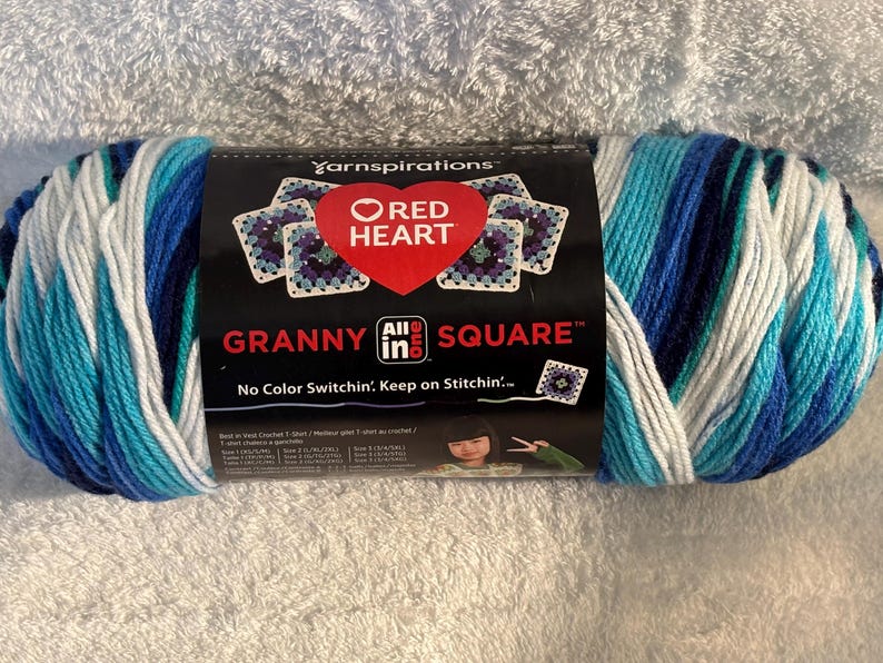 Pode incluir: Um novelo de fio Red Heart Granny All in One Square com uma paleta de cores variadas em branco, azul claro, azul m&eacute;dio e azul escuro. O r&oacute;tulo preto do produto exibe o nome da marca, o log&oacute;tipo e o texto No Color Switchin'.