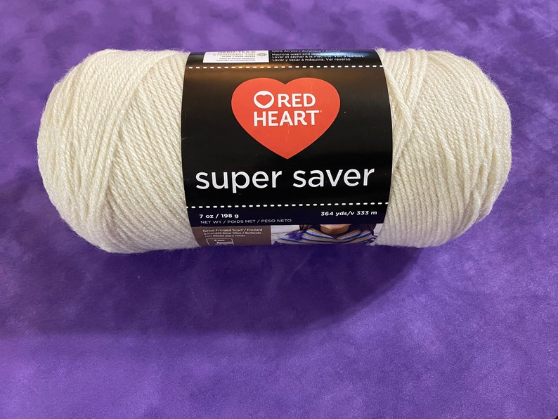 May include: A skein of off-white yarn with a black label featuring a red heart logo and the text Red Heart Super Saver. The label indicates a net weight of 7 ounces and a length of 364 yards. The yarn is wound into a cylindrical shape.