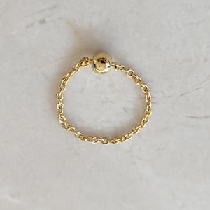 May include: A gold chain ring with a small, round bead in the centre.
