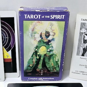 May include: A Tarot of the Spirit card deck with a purple box and several cards. The box features an illustration of a figure in green robes. The cards have the text "Tarot of the Spirit" and various illustrations. The deck is by U.S. Games Systems, Inc.