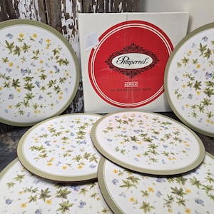 Peut inclure: Ensemble de six sets de table ronds en acrylique avec un motif floral. Les sets de table présentent un fond blanc avec des fleurs vertes, jaunes et bleues et des feuilles vertes. Les sets de table ont une bordure vert clair. La boîte indique "Pimpernel" et "Six Round Place Mats".