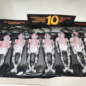 May include: A string of 10 skeleton-shaped lights with clear plastic bodies and red ribcage details, connected by a black wire. The packaging features the text "10 SKELETON LIGHT SET" and "WITH TWINKLING CONTROL BOX" in orange and white lettering.