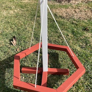 May include: A red wooden hexagonal frame with a white wooden pole in the center. The frame is suspended from the pole by white ropes.