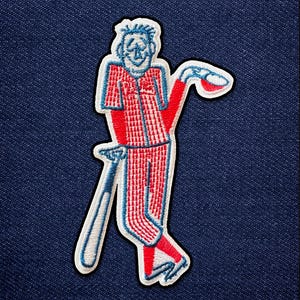 May include: Embroidered patch featuring a baseball player in a red and white striped uniform, holding a bat and a baseball cap. The patch has a white border and is set against a dark blue denim background. The player's uniform has the number 22.