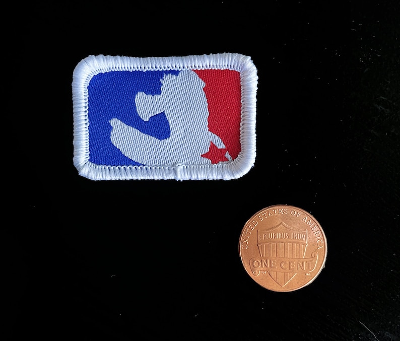 May include: A rectangular patch featuring the MLB logo in red, white, and blue. The patch is bordered with white stitching. A US one-cent coin is next to the patch for size comparison.