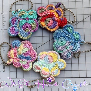 May include: Five crocheted flower charms in various colors, including pink, blue, green, and yellow. Each charm has a loop for attaching to a keychain or bag.