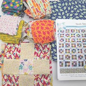 Może przedstawiać: Kolekcja kolorowych kwadratów materiału i kawałków materiału we wzory, w tym niebieski nadruk w liście i przewodnik po wzorach pikowania. Przewodnik nosi tytuł "Ninth Square" i pokazuje wzór pikowania. Kwadraty materiału są w różnych kolorach i wzorach.