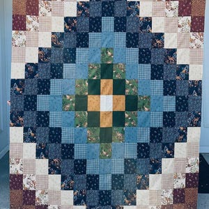 Può includere: Una trapunta patchwork quadrata composta da una griglia di quadrati di tessuto nelle tonalità blu navy, azzurro, verde bosco, giallo senape, crema e bordeaux. Il design incorpora vari motivi, tra cui quadri, fiori e stampe di animali del bosco.