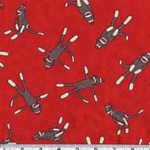 May include: A red fabric featuring a repeating pattern of brown sock monkeys. Each monkey has a white face, white hands, and white feet, with a red cap on its head. The monkeys are oriented in various directions across the vibrant red background.