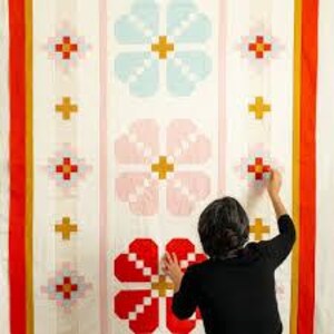 Puede incluir: Un edredón grande y colorido con un estampado floral. El edredón presenta grandes flores estilizadas en tonos de rojo, rosa y azul, con acentos amarillos y naranjas. El edredón está colgado en una pared, y una persona lo está ajustando.