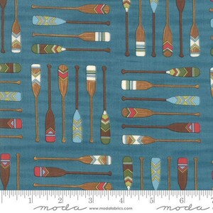Peut inclure: Un tissu bleu sarcelle avec un motif répétitif de pagaies de canoë en bois aux motifs géométriques colorés sur les pales. Les pagaies sont orientées horizontalement et verticalement. Une règle blanche est visible sur le bord inférieur.