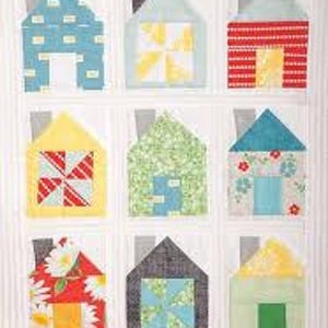 Puede incluir: Una colcha con un diseño de patchwork que presenta nueve casas en varios colores y patrones. Cada casa tiene una chimenea y un diseño diferente en la parte delantera, incluyendo un molino de viento, una flor y una puerta.