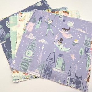May include: A stack of fabric squares with a whimsical Peter Pan theme. The fabrics feature illustrations of Peter Pan, Wendy, and Captain Hook, along with London landmarks in shades of blue, lavender, and green. The fabric is likely cotton.
