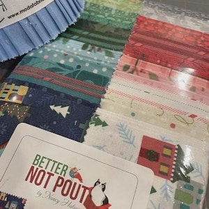 Op de afbeelding: Een verzameling stoffen stroken in diverse kleuren en patronen, waaronder groen, blauw en rood. Een blauwe meetlint is zichtbaar linksboven. Het label luidt "BETTER NOT POUT" en bevat een kattenillustratie. De stoffen stroken zijn 6,35 cm breed.