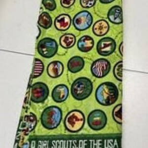 Puede incluir: Tela verde con un patr&oacute;n repetido de insignias de Girl Scouts en c&iacute;rculos blancos y marrones. La tela tiene el texto "Girl Scouts of the USA" y un n&uacute;mero de tropa.
