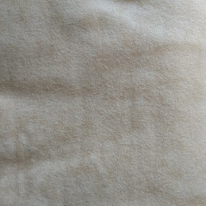 Könnte beinhalten: Nahaufnahme eines beigefarbenen Stoffes mit weicher, strukturierter Optik. Das Material weist subtile Farbvariationen auf, die ein sanftes, fließendes Muster erzeugen. Der Stoff wirkt weich und bequem.