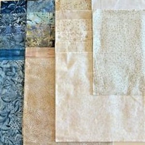 Può includere: Una collezione di quadrati di tessuto in varie tonalità di blu, beige e crema. I tessuti presentano motivi floreali e maculati, adatti per progetti di quilting o artigianato. La disposizione mostra le diverse trame e design.