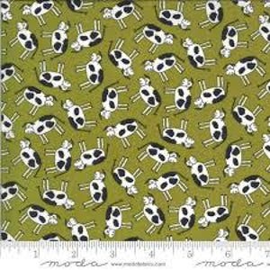 May include: Green fabric with a repeating pattern of black and white cartoon cows. The cows are in various poses against a solid green background. A ruler is at the bottom of the image.