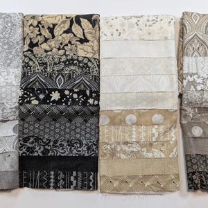 Peut inclure: Quatre piles de tissus aux motifs et couleurs variés. Les tissus présentent des motifs floraux, cachemire et géométriques dans des tons de gris, noir et beige. Les tissus sont disposés en bandes horizontales.