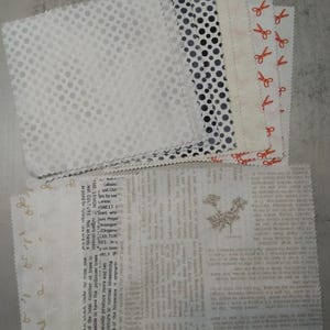 May include: A collection of fabric swatches in various patterns. Designs include white with small dots, black and gray polka dots, and a cream-colored fabric with red scissors. Other swatches feature text and floral patterns.