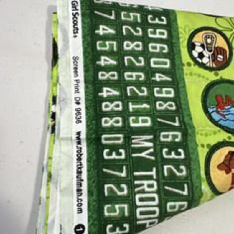 Puede incluir: Tela verde con un patr&oacute;n repetido de insignias de Girl Scout y el texto "MY TROOP" y n&uacute;meros. La tela es de Robert Kaufman Fabrics y tiene el n&uacute;mero de producto D 9638.