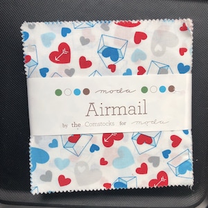 Puede incluir: Un cuadrado de tela blanco con un patrón repetido de corazones rojos, azules y grises, sobres y flechas. La tela está etiquetada como "moda Airmail by the Comstock for moda".