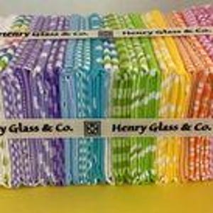 May include: A stack of colorful fabric squares with a white background and a repeating pattern of small white dots. The fabric is bundled together with a ribbon that reads "Henry Glass & Co."