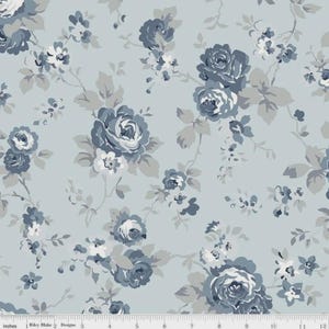 May include: A light blue fabric featuring a repeating floral pattern of dark blue and grey roses with green-grey leaves. A white ruler is visible at the bottom edge, showing measurements in inches from 0 to 12, with the text Riley Blake Designs.