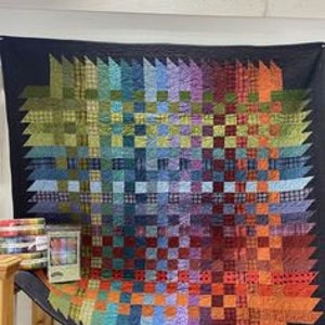 Pode incluir: Um cobertor colorido com um padrão geométrico de quadrados e triângulos. O cobertor é feito com uma variedade de tecidos em tons de azul, verde, vermelho e laranja.
