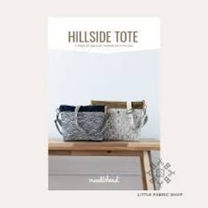 May include: Two tote bags, one white with black and gray stripes and one black with white and gray stripes, are displayed on a wooden table. The bags have a brown leather strap and are labeled "Hillside Tote".