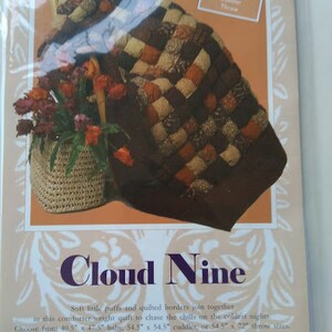 May include: A quilt pattern called "Cloud Nine" with a patchwork design in shades of brown, orange, and cream. The quilt is available in three sizes: baby, cuddler, and throw.