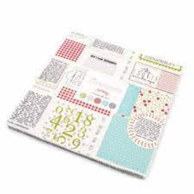 May include: A white fabric with a patchwork design featuring red and white gingham, blue and white polka dots, and a variety of text and numbers. The fabric also includes a small red and white heart pattern.