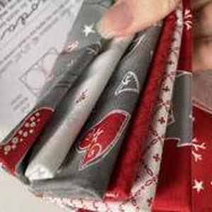 Peut inclure: Un lot de cinq carrés de tissu sur le thème de Noël. Les tissus sont de couleur rouge, blanc et gris avec différents motifs, notamment des étoiles, des cœurs et des flocons de neige.